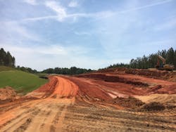 Topsoil and permanent vegetation are applied as roadway cut slopes are excavated to grade on the US 98 project. A completed section of the roadway is beyond the active work area. Topsoil and permanent vegetation are applied as roadway cut slopes are excavated to grade on the US 98 project. A completed section of the roadway is beyond the active work area.