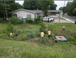 Crew maintaining rain garden next to Community Enhancement food garden with cistern.