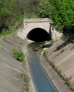 A concrete culvert in an elliptical shape conveying water down a concrete spillway.